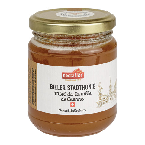 Glas mit goldfarbenem Deckel und weißem Etikett mit der Aufschrift 'nectaflor BIELER STADTHONIG Miel de la ville de Bienne Finest Selection' und einer Zeichnung von Gebäuden