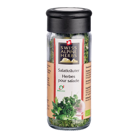 Transparente Gewürzmühle mit schwarzem Deckel. Auf dem Etikett steht „Salatkräuter / Herbes pour salade“ unter dem Swiss Alpine Herbs Logo. Im Glas sind grüne Kräuter sichtbar. Unten sind Kräuter, eine rote Zwiebel sowie das Bio-Suisse-Logo abgebildet.