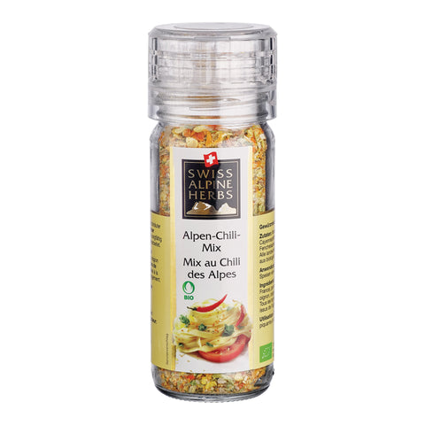 Transparente Gewürzmühle mit durchsichtigem Deckel. Auf dem Etikett steht „Alpen-Chili-Mix / Mix au Chili des Alpes“ unter dem Swiss Alpine Herbs Logo. Im Glas sind grobe Kräuter und Gewürze sichtbar. Unten sind Nudeln, eine rote Chilischote, eine Tomatenscheibe sowie das Bio-Logo abgebildet.