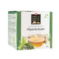 Grüne Verpackung mit der Aufschrift 'Swiss Alpine Herbs Alpenkräutertee Alpenkräuter' und einem Glas mit hellem Kräutertee