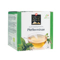 Grüne Verpackung mit der Aufschrift 'Swiss Alpine Herbs Alpenkräutertee Pfefferminze' und einem Glas mit hellem Tee sowie Pfefferminzblättern